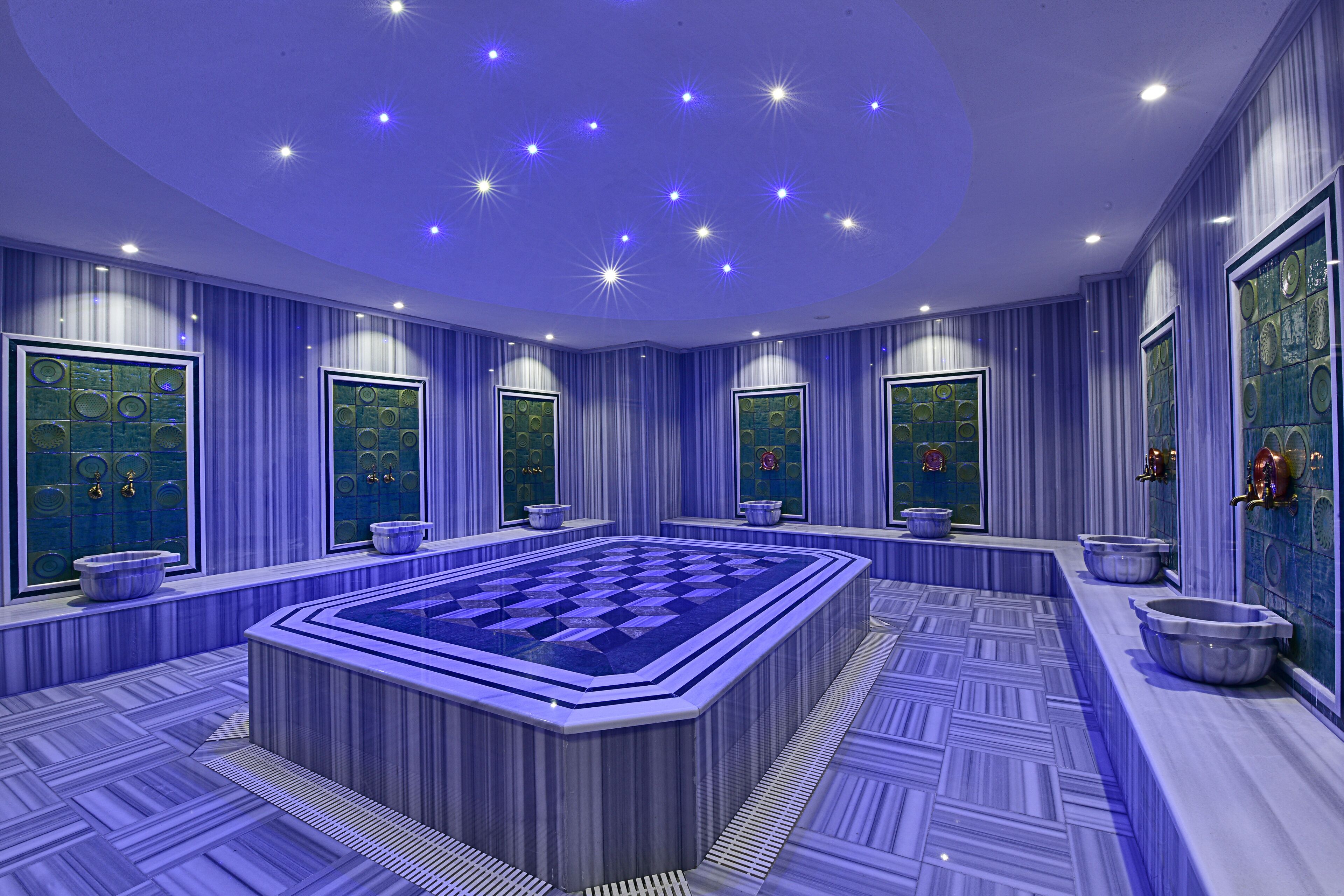 Une salle de bain luxueuse dotée d’une grande baignoire centrale, de plusieurs lavabos et de miroirs décoratifs.