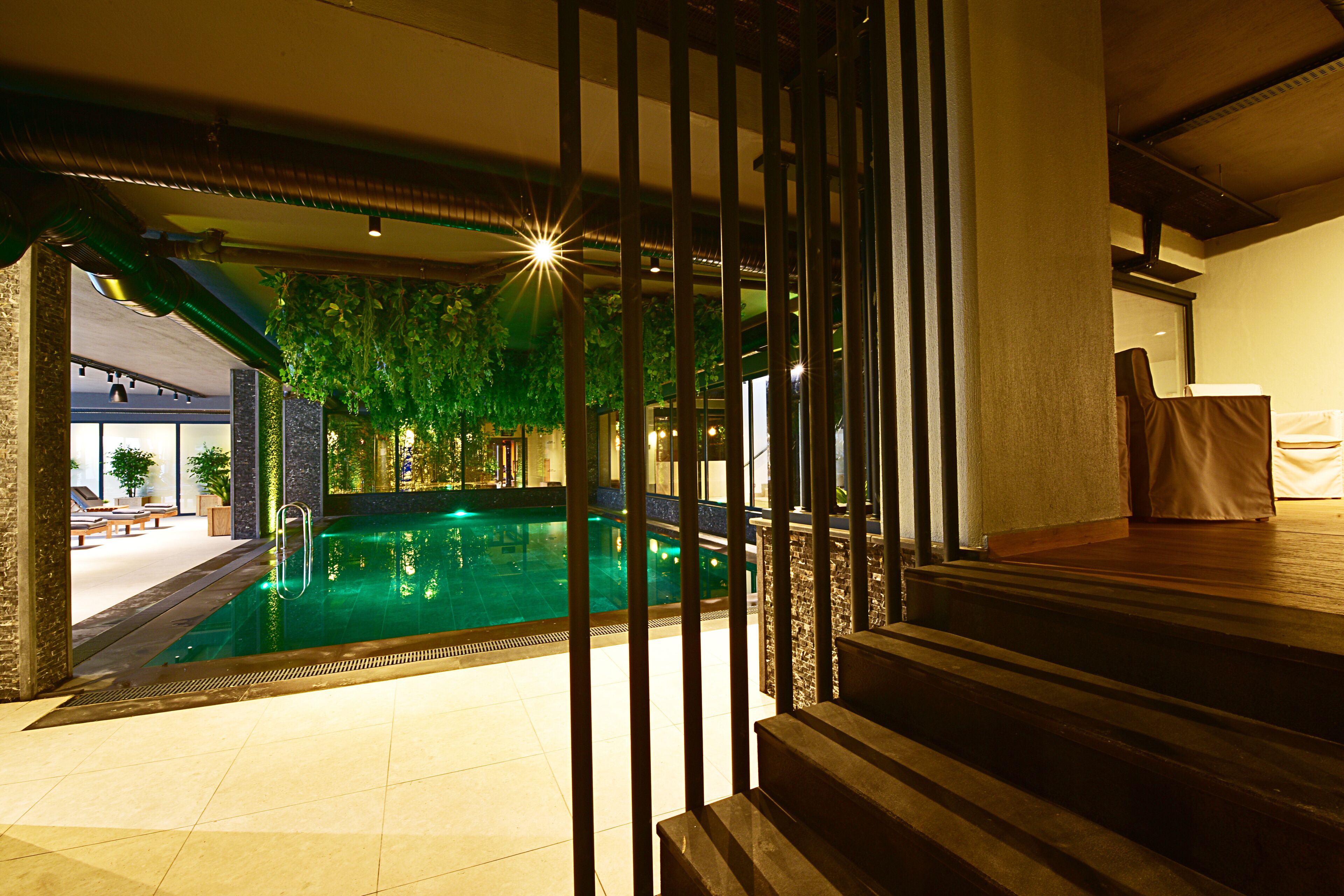 An indoor swimming pool with a view of a lounge area and a staircase leading to another level.