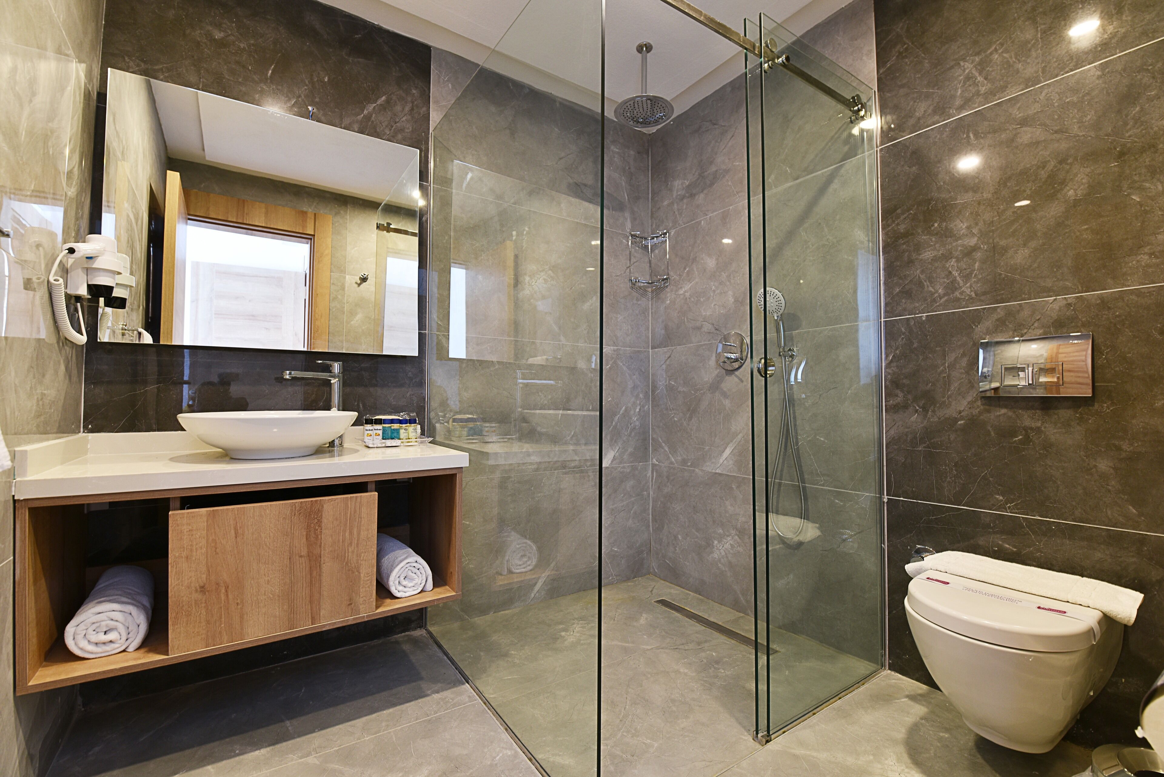 A modern bathroom with a glass-enclosed shower, a white sink, and a wooden vanity.