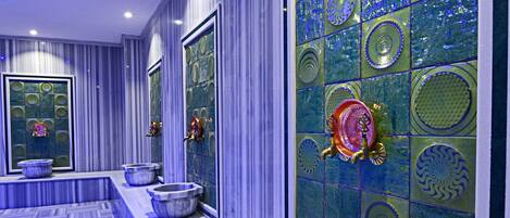 Un baño largo y estrecho con piso y paredes de mármol, que presenta un espejo decorativo grande y un lavabo con una pileta ornamental.
