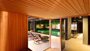 Een modern binnenzwembad met houten vloer, lounge stoelen en een glazen wand.