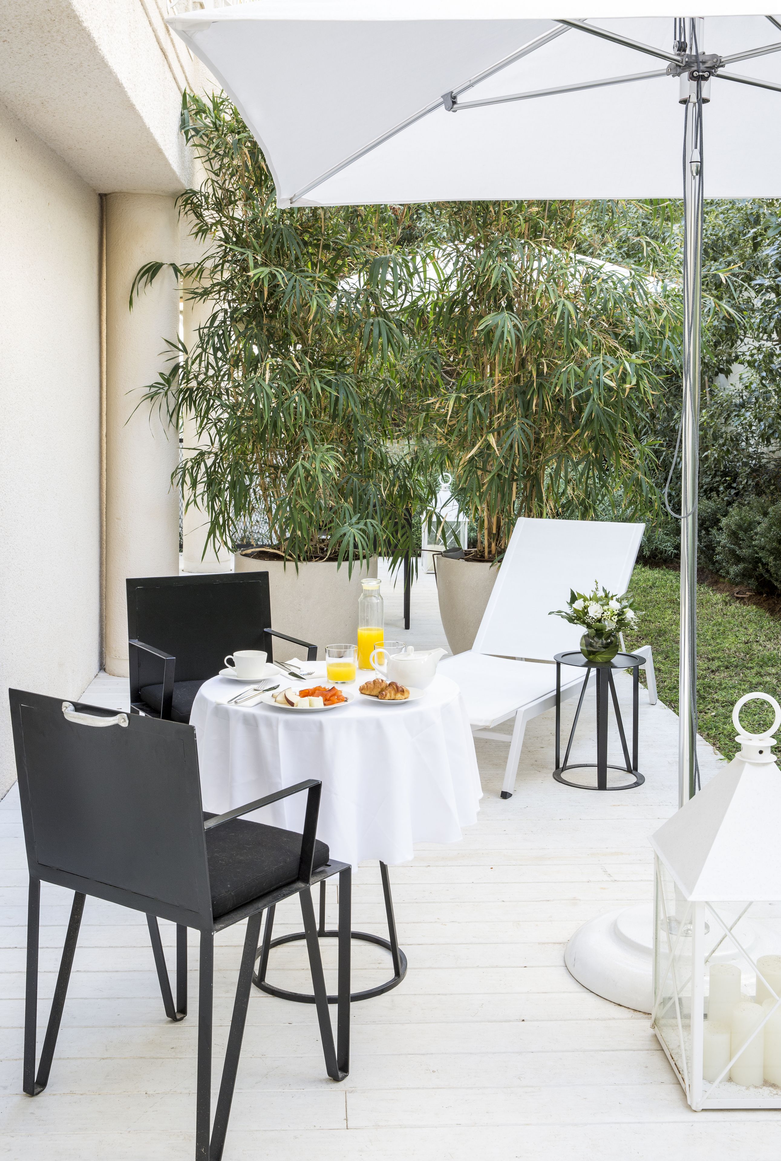 An outdoor patio with a table set for breakfast, surrounded by chairs, a potted plant, and a white lantern.