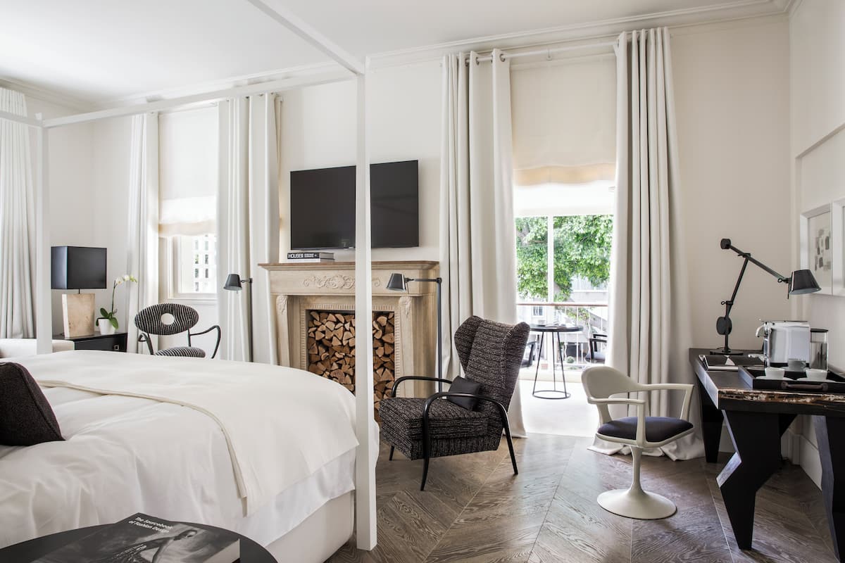 Habitación de hotel con una cama grande, chimenea, televisión, escritorio con lámpara y vista al exterior.