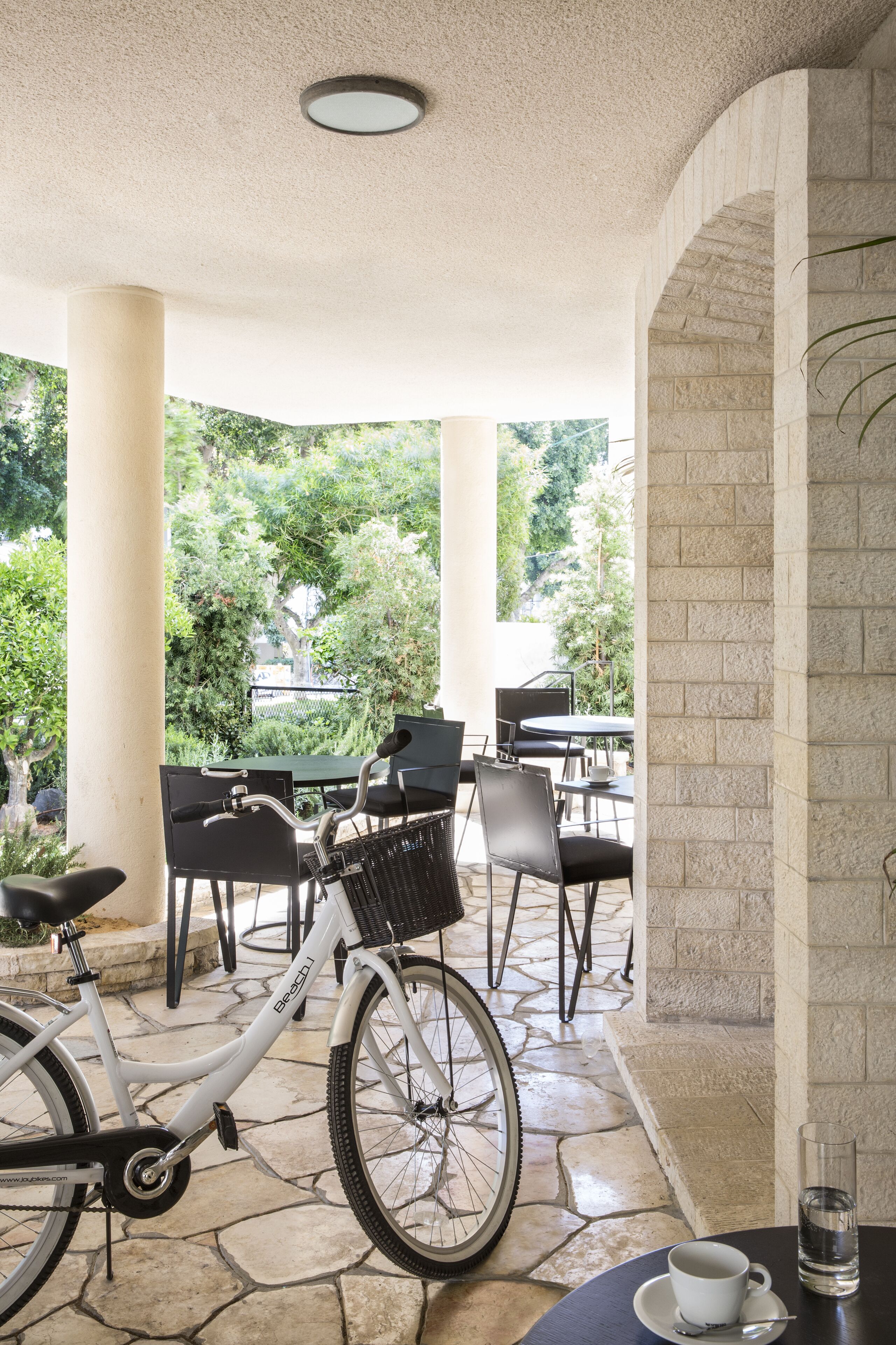 A covered outdoor seating area with stone flooring, a white bicycle, and tables with chairs.