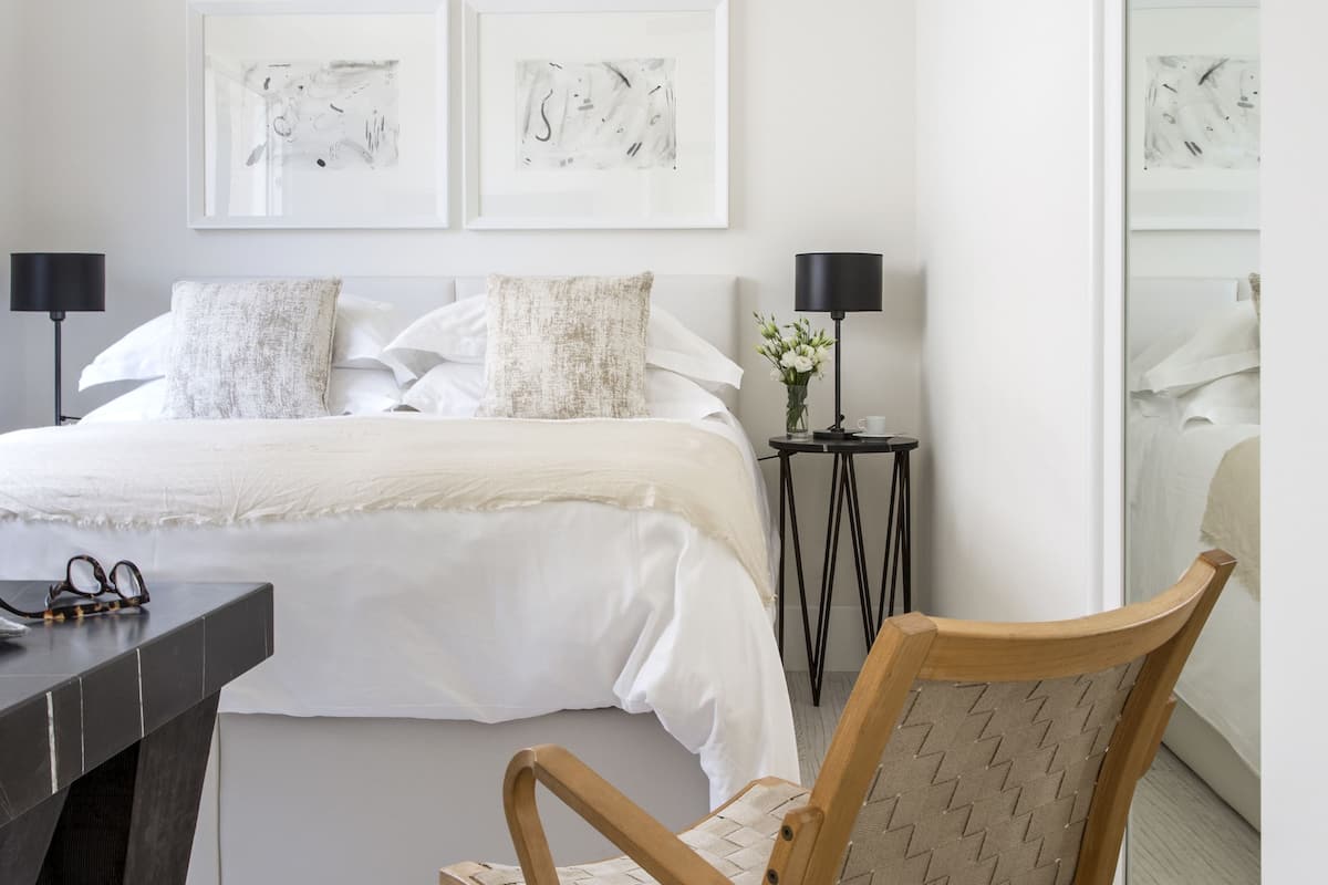 Un dormitorio con cama, una silla de madera, una mesita y una mesita de noche.
