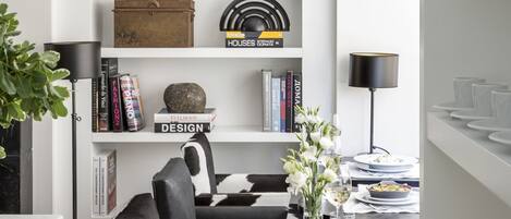 A modern living room with a black and white sofa, a dining table with plates and glasses, and a bookshelf with books and decorative items.