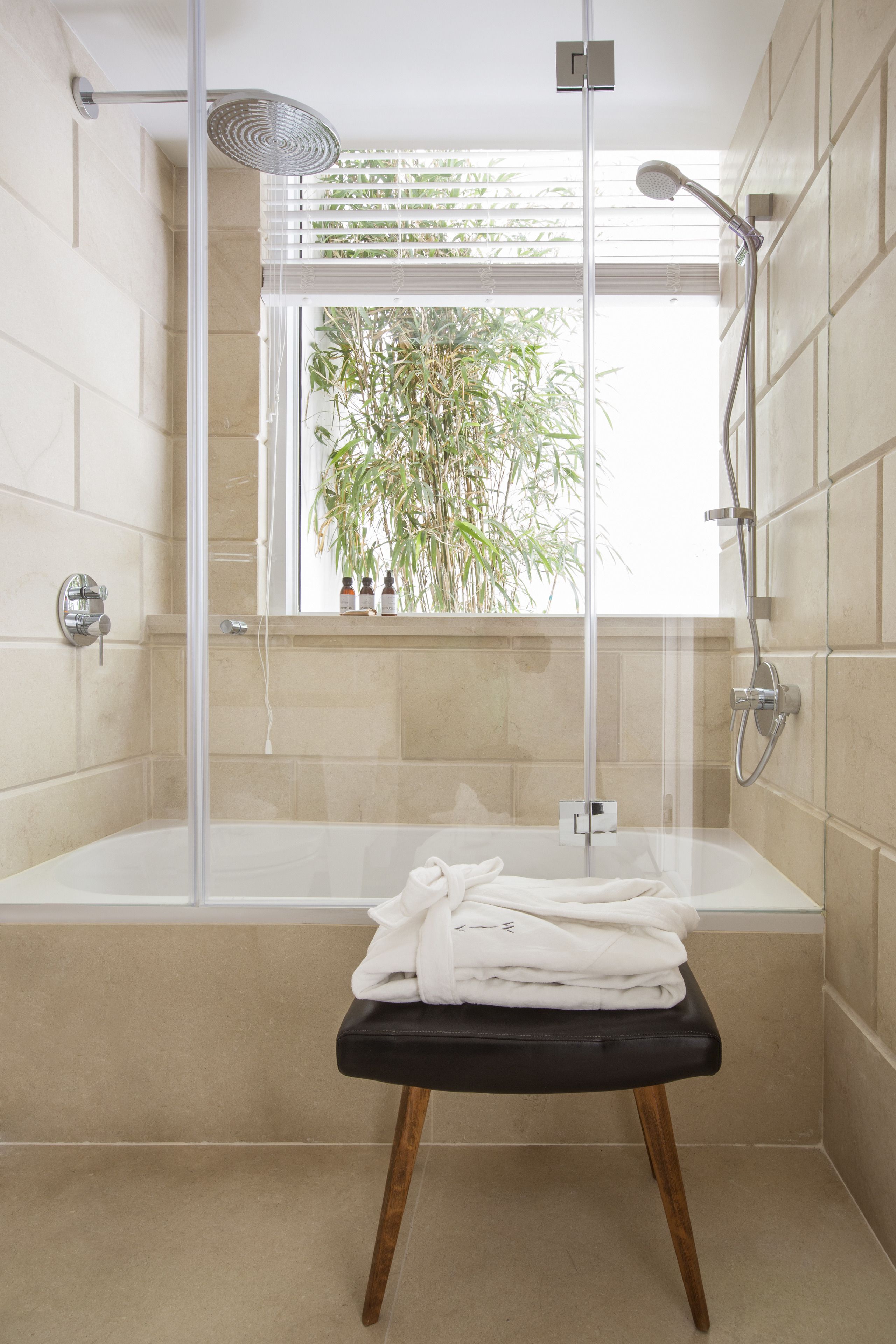 A modern bathroom with a glass-enclosed shower, a bathtub, and a window with a view of greenery.