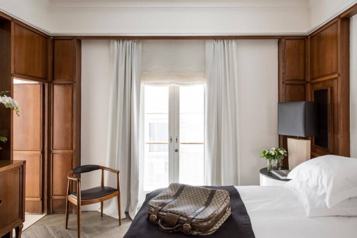 Habitación de hotel con cama, una silla, escritorio, televisor y ventana con cortinas.
