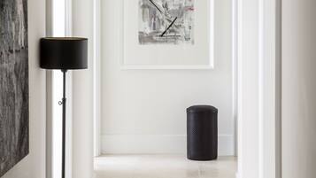 A hallway with a bench, a framed abstract painting, a floor lamp, and a trash can.