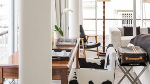 Une chambre d’hôtel moderne dotée d’une grande fenêtre, d’un bureau en bois, d’un fauteuil confortable, d’un canapé et d’un balcon avec une balustrade.