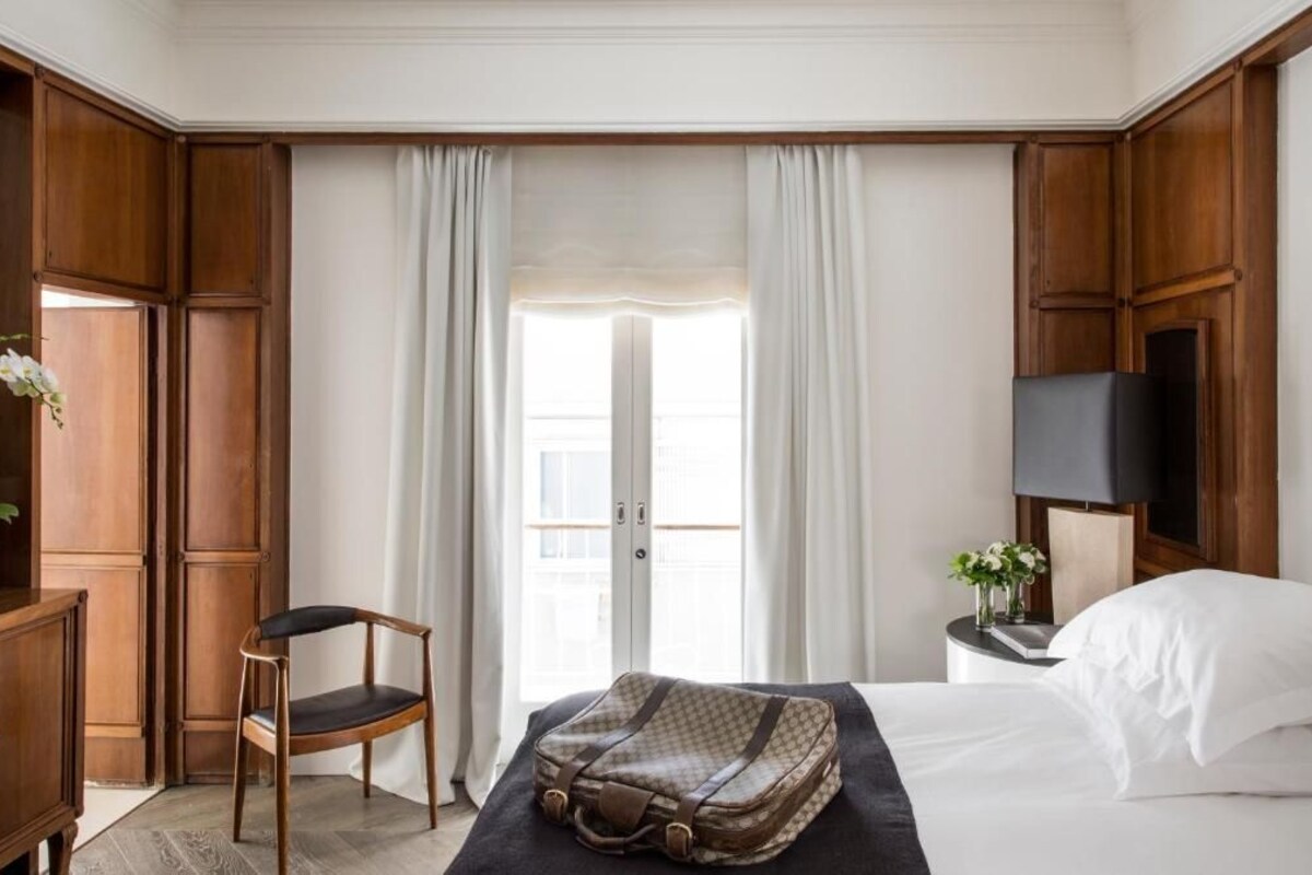 Ein Hotelzimmer mit Bett, Stuhl, Schreibtisch, Fernseher und einem Fenster mit Vorhängen.