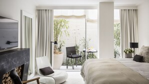 Une chambre d’hôtel moderne dotée d’un grand lit, d’une télévision, d’une cheminée, d’un balcon avec vue sur la plage et d’une petite table avec une chaise.