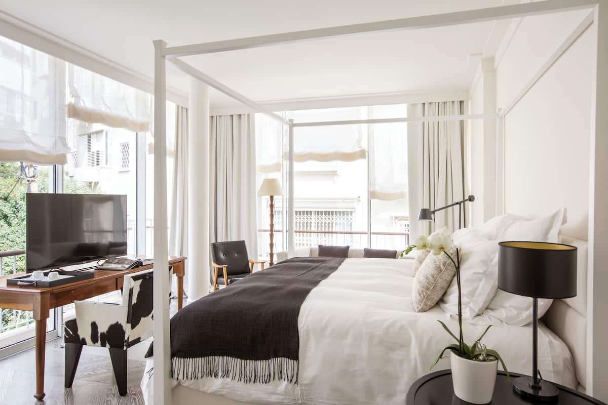 Habitación de hotel moderna con una cama grande, un escritorio con computadora, televisor y balcón con vistas a la ciudad.