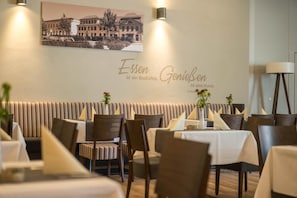 A restaurant interior with striped booths, tables with white tablecloths, and a wall with a framed picture and text.