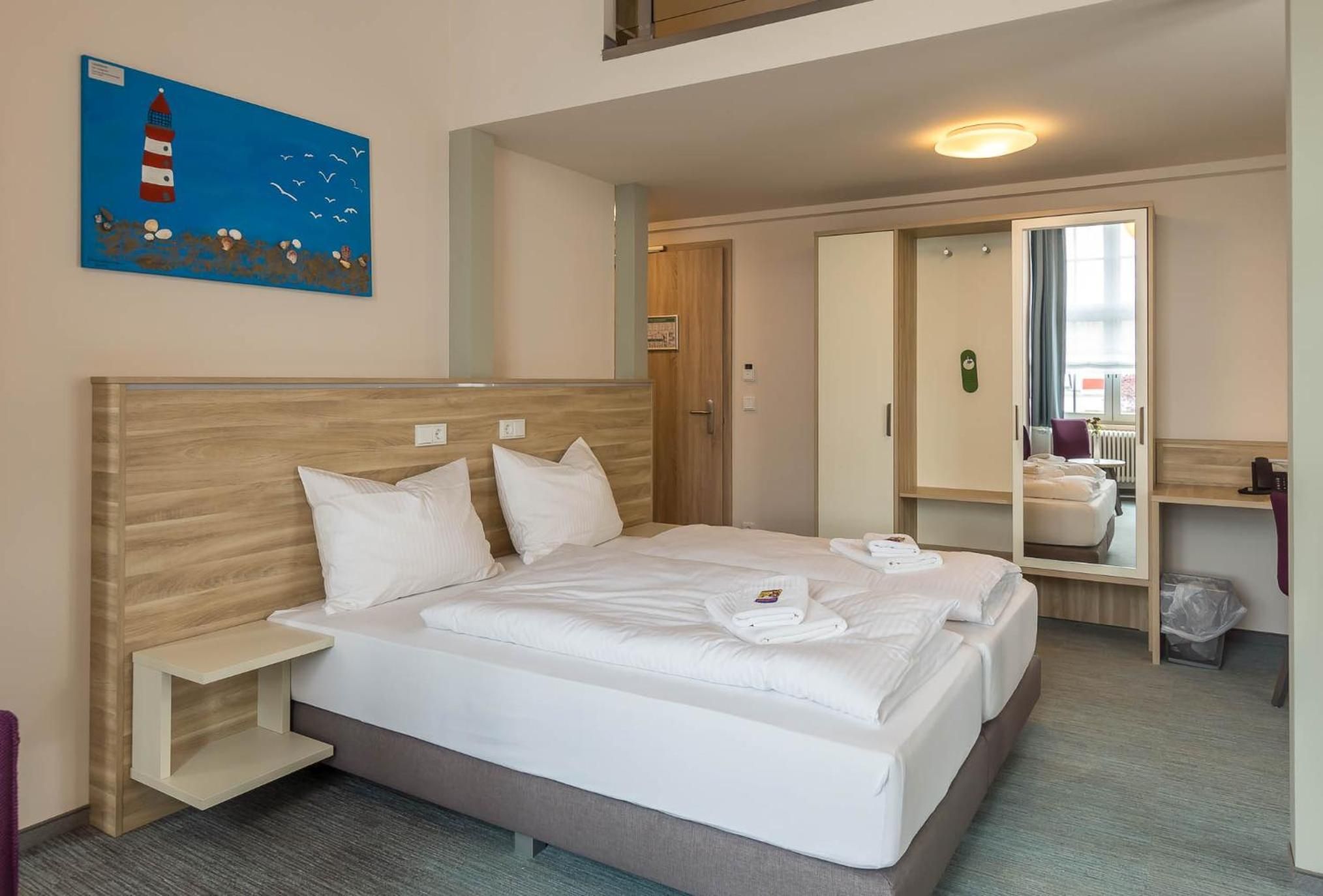 A hotel room with a bed, a nightstand, a mirror, and a painting on the wall.
