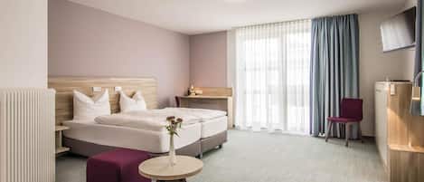 A hotel room with a bed, a bedside table, a chair, a small table, and a TV.