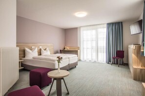 A hotel room with a bed, a bedside table, a chair, a small table, and a TV.