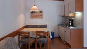 A compact kitchen with wooden cabinets, a dining table with chairs, a hanging pendant light, and a painting on the wall. - Landhaus Aggenstein (Graen)