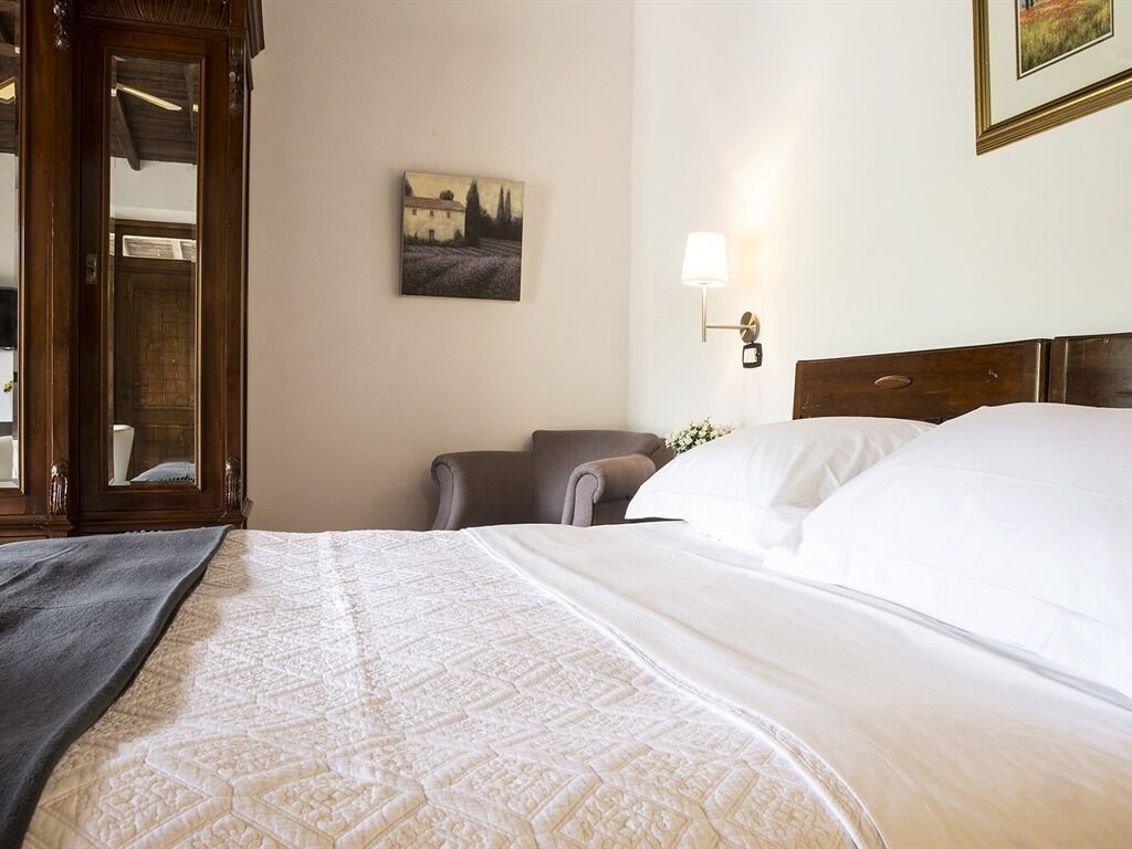 A hotel room with a bed, a chair, a lamp, and a painting on the wall.