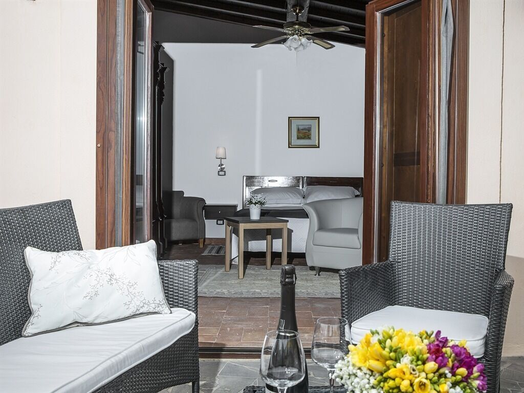 Quarto com mobiliário de vime, cama, mesa com uma garrafa e um vaso de flores.