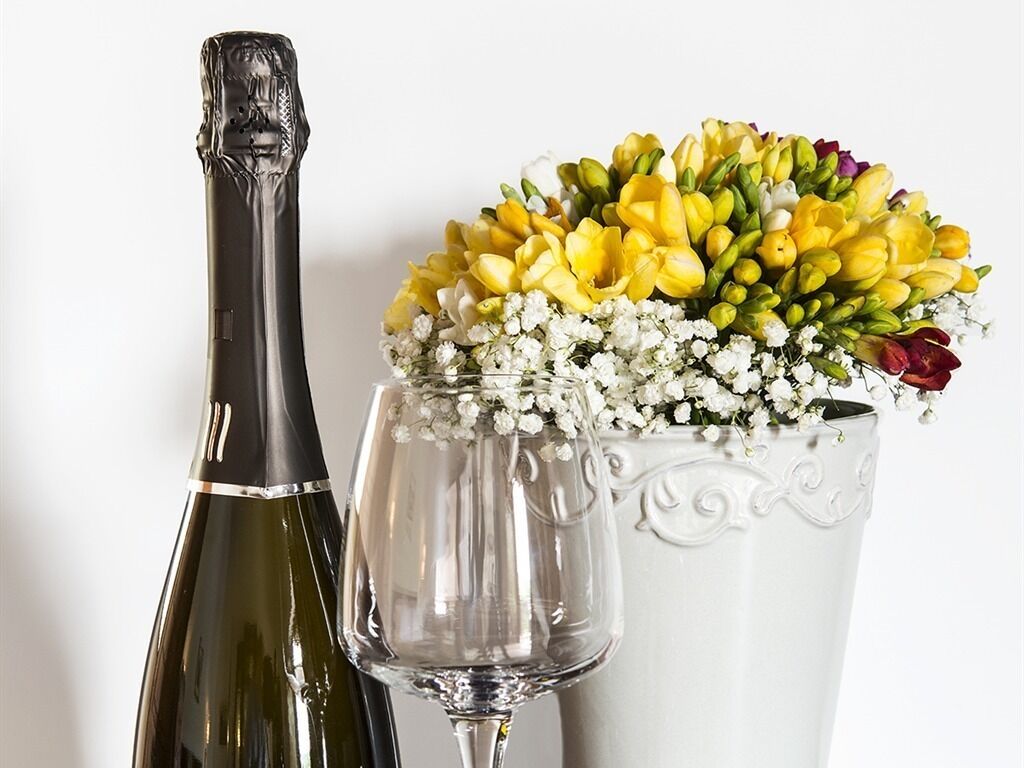 A wine bottle, a wine glass, and a vase with flowers.