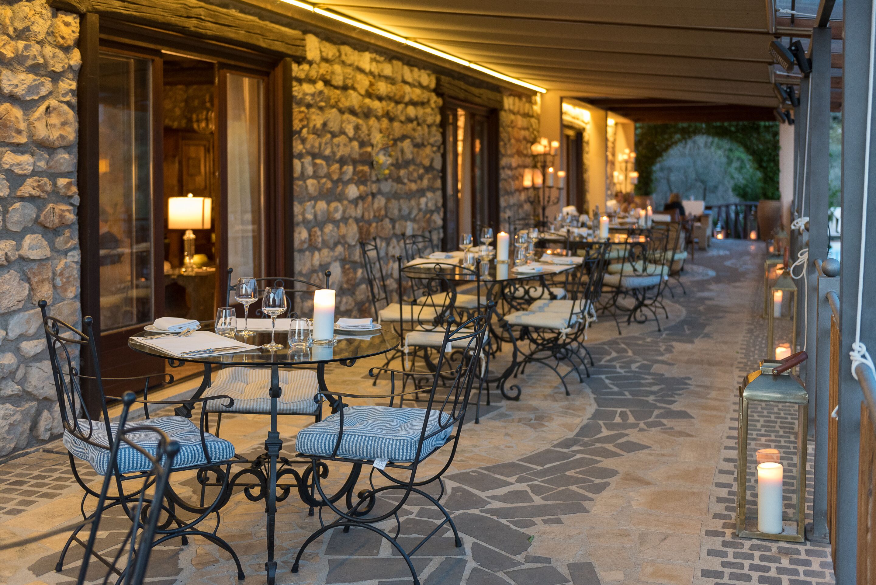 Un espace extérieur aménagé pour les repas, avec des murs en pierre, des tables et des chaises en métal.
