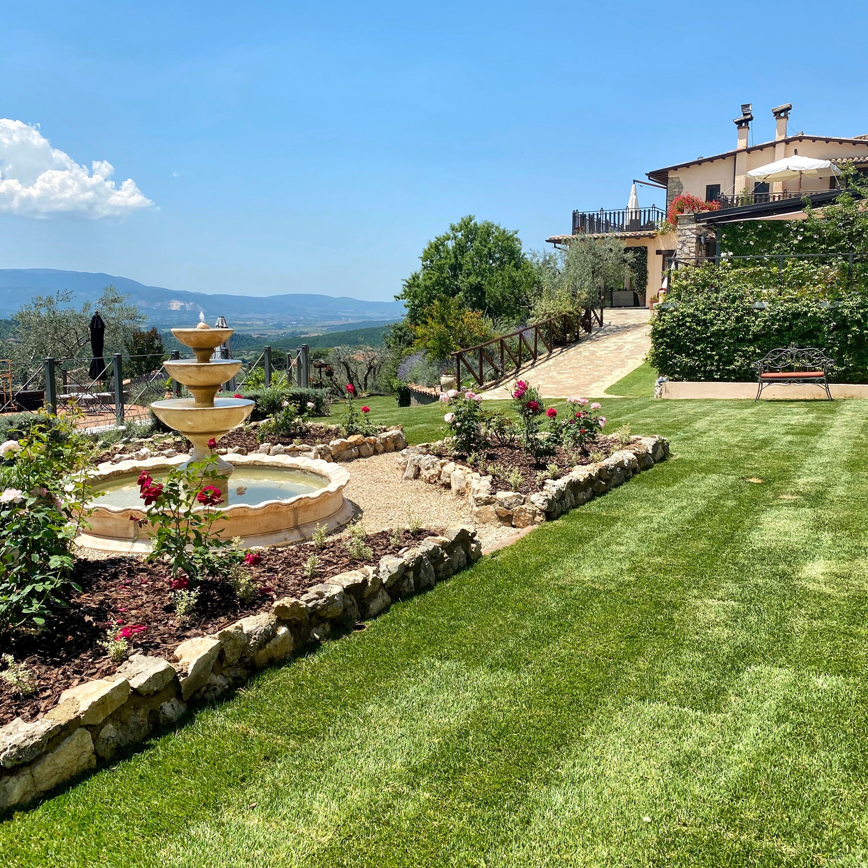 A landscaped garden with a fountain, a well-maintained lawn, and a building with a balcony.