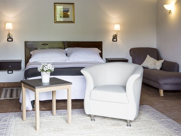 Une chambre d’hôtel avec un lit, un fauteuil blanc, une petite table avec un vase, deux tables de chevet et des lampes fixées au mur.