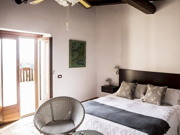 A bedroom with a bed, a chair, a nightstand, a painting, and a sliding door to the outside. - Casale San Pietro (Anagni)