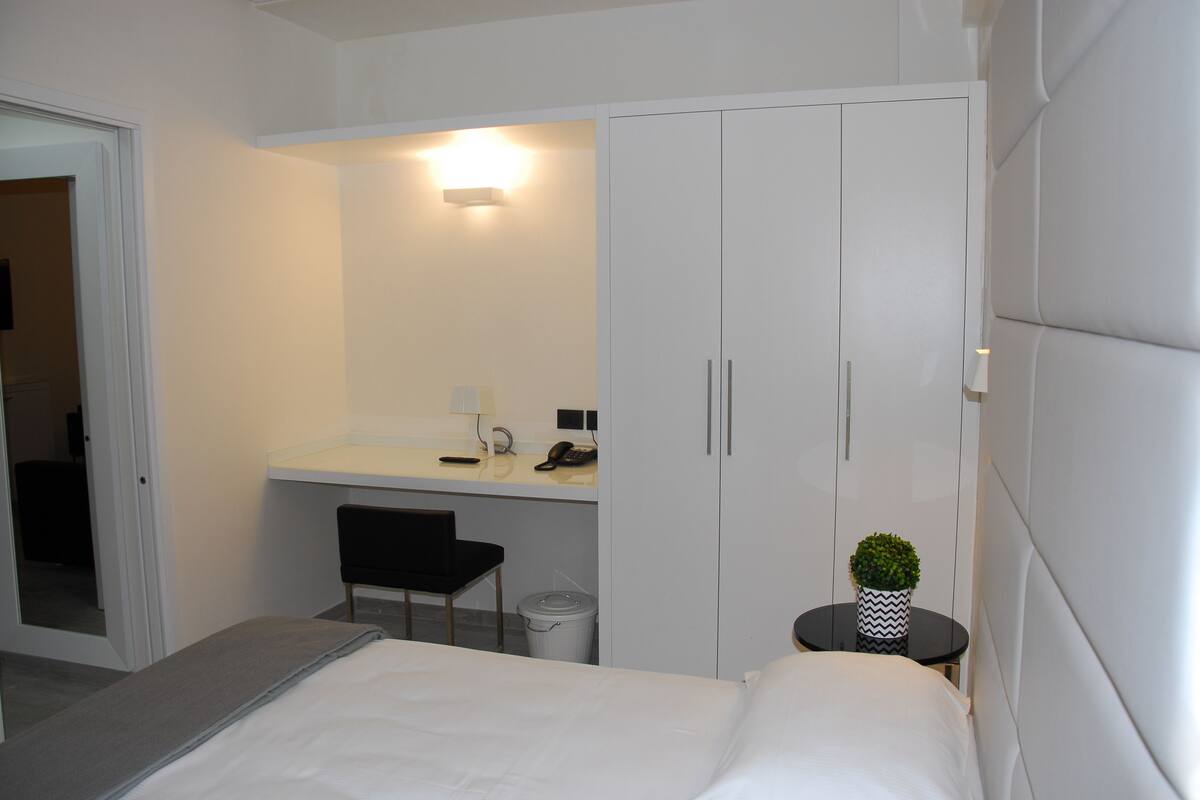 Una habitación de hotel moderna con una cama, un escritorio, una silla, una mesita con una planta y un armario.