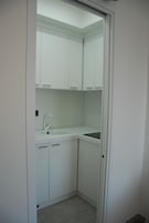 Un baño pequeño y blanco con lavamanos, armarios y espejo.