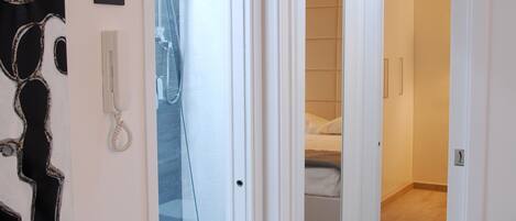 A hotel corridor with a bathroom, a bedroom, and a shower area.