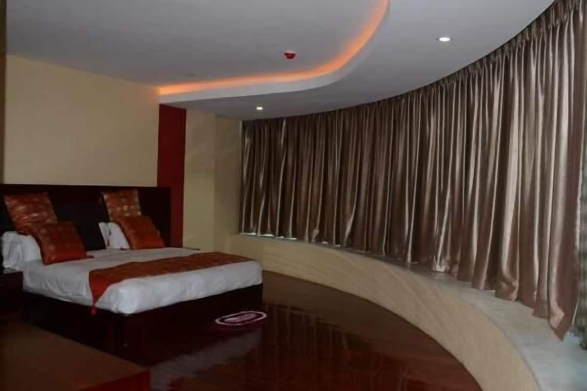 A modern hotel room with a curved ceiling, a large bed with red and white bedding, and a view of a curtain-covered window.