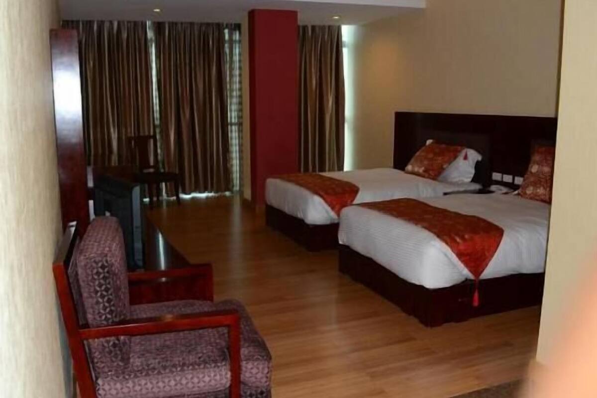 A hotel room with two beds, a desk, a chair, and a view of the outside through large windows.