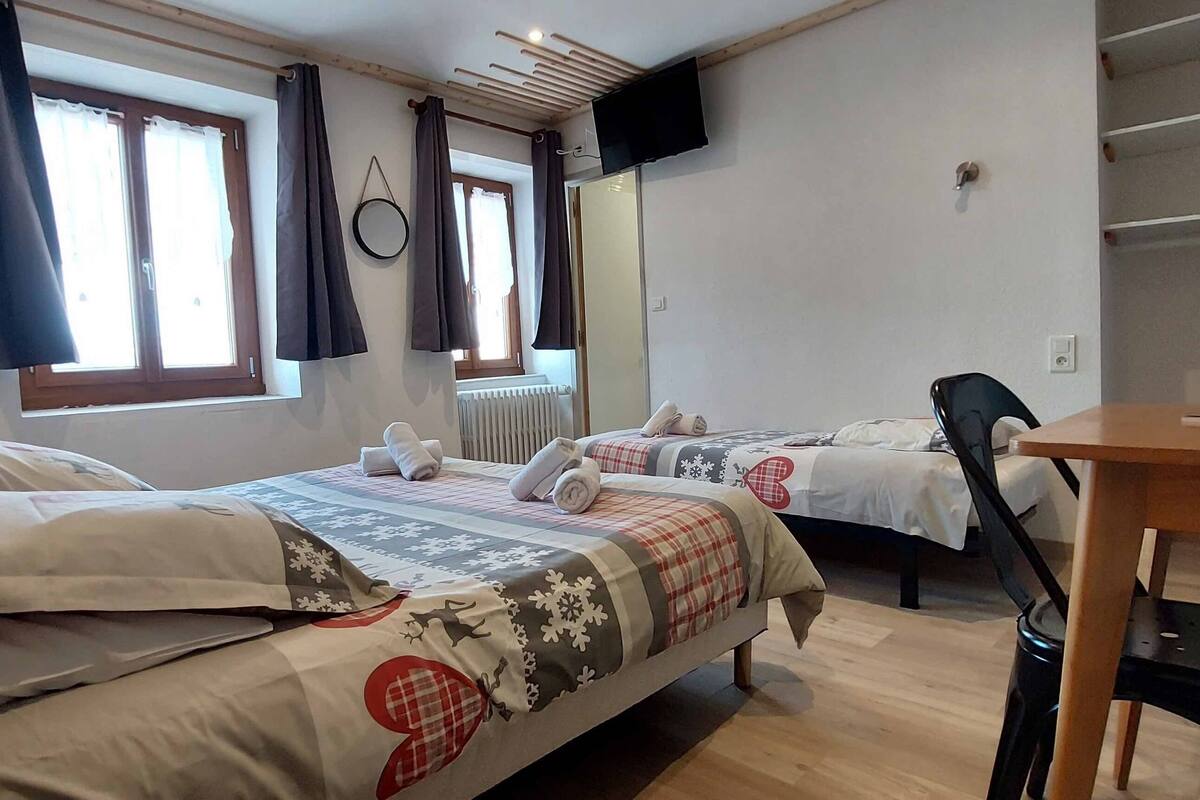 A hotel room with two beds, a wooden desk, a chair, a TV, and a window with curtains.
