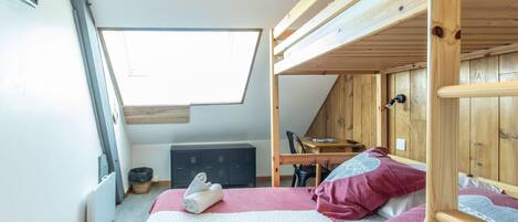 A room with a bunk bed, a desk, and a window.
