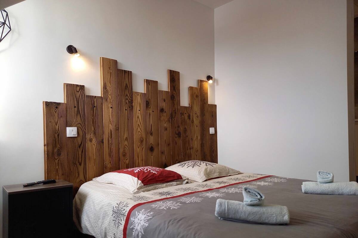 A bedroom with a wooden headboard, a bed with a grey and white patterned bedspread, and two bedside lamps.