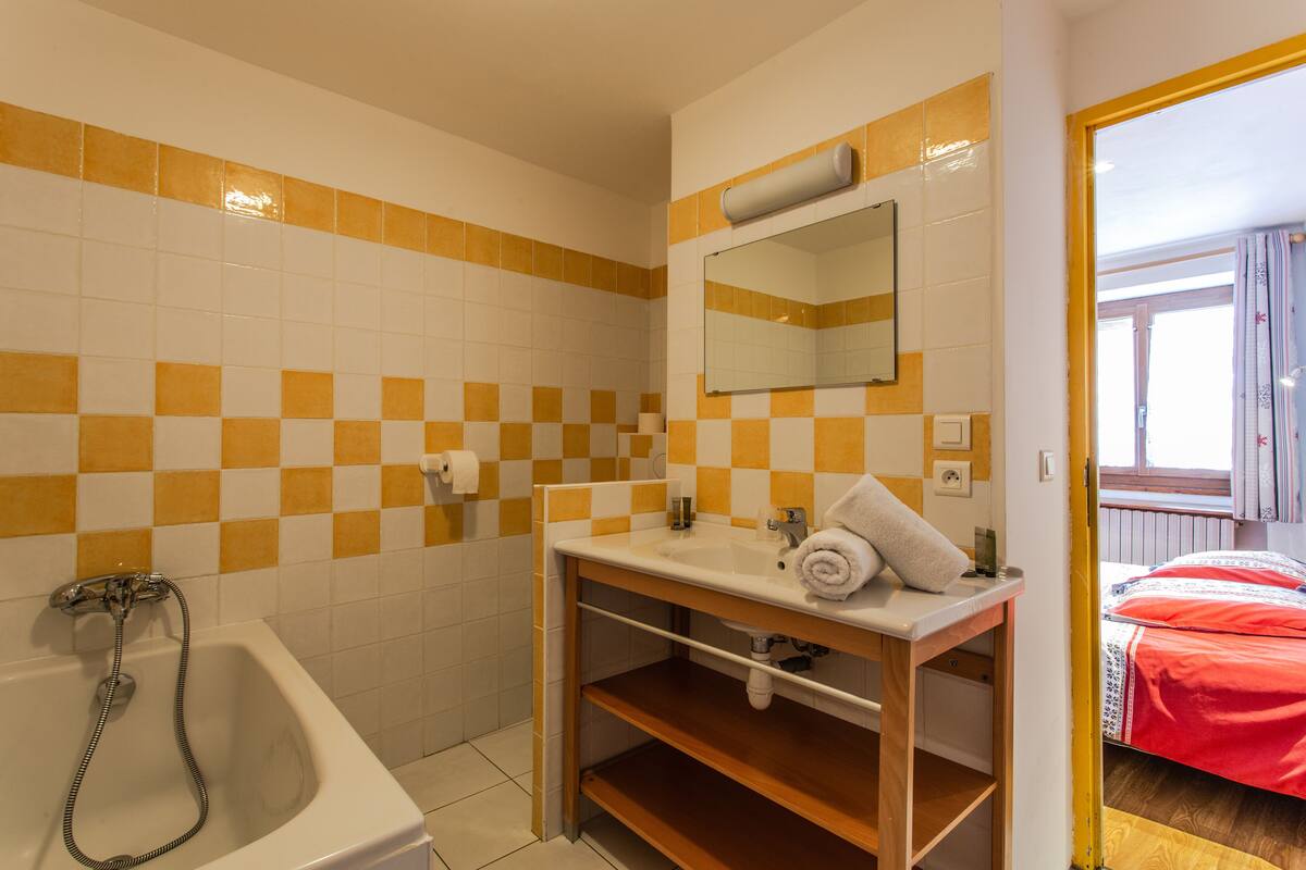 A bathroom with a checkered yellow and white tile wall, a white sink with a mirror, a towel, and a bathtub with a shower hose.