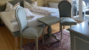 Un dormitorio con cama, una silla, una mesita, un radiador y una ventana con cortinas.