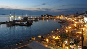 Un puerto deportivo costero con barcos amarrados, un puente al fondo y un paisaje urbano con edificios e iluminación de calles.