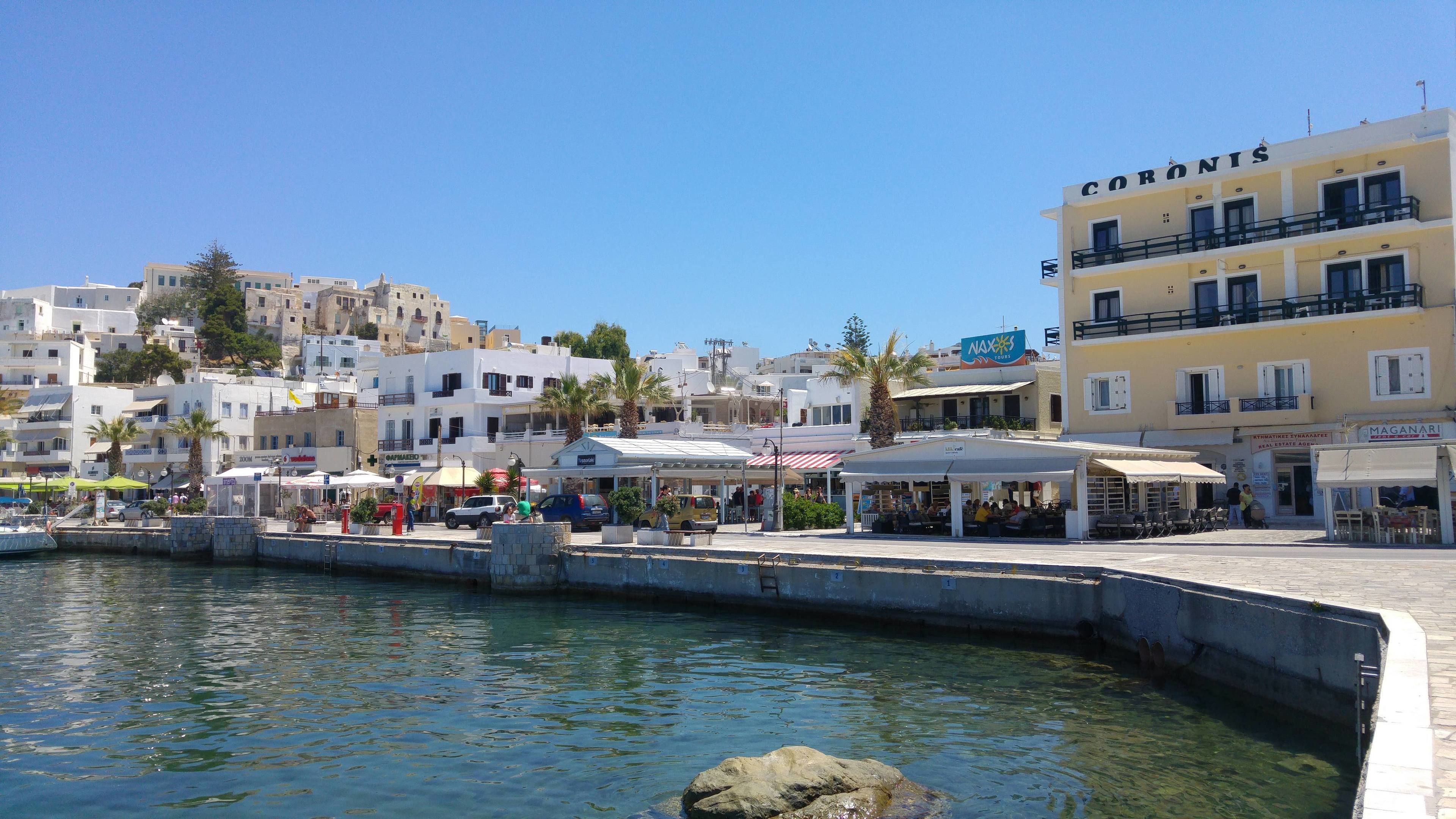A coastal town with a marina, buildings with balconies, and outdoor seating areas.