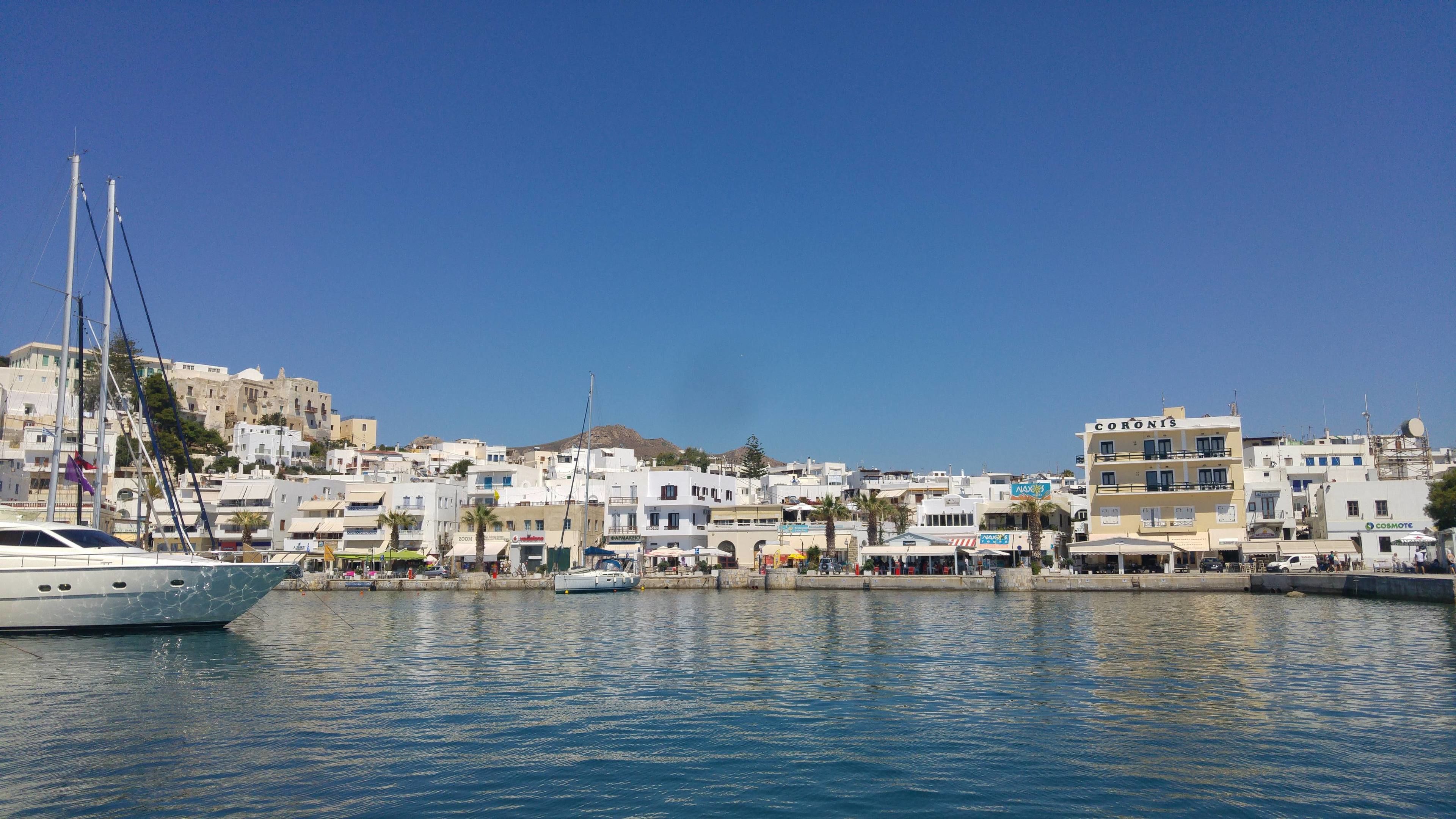 Un puerto deportivo con barcos y un pueblo costero con edificios blancos y una colina al fondo.