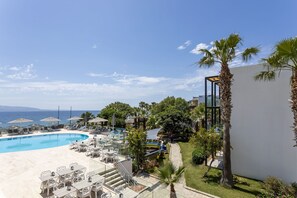 Un espace piscine aménagé dans un complexe hôtelier, avec des chaises longues, des parasols et une vue dégagée sur l’océan.