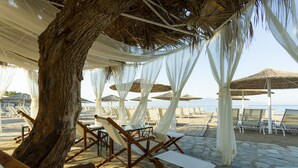 A beachside lounge area with wooden lounge chairs and thatched umbrellas, set against a backdrop of a clear sky and a distant shoreline. - Charm Beach Hotel - All Inclusive (Bodrum)