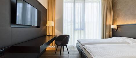 A hotel room with a bed, a desk, a chair, a TV, and a window with curtains.