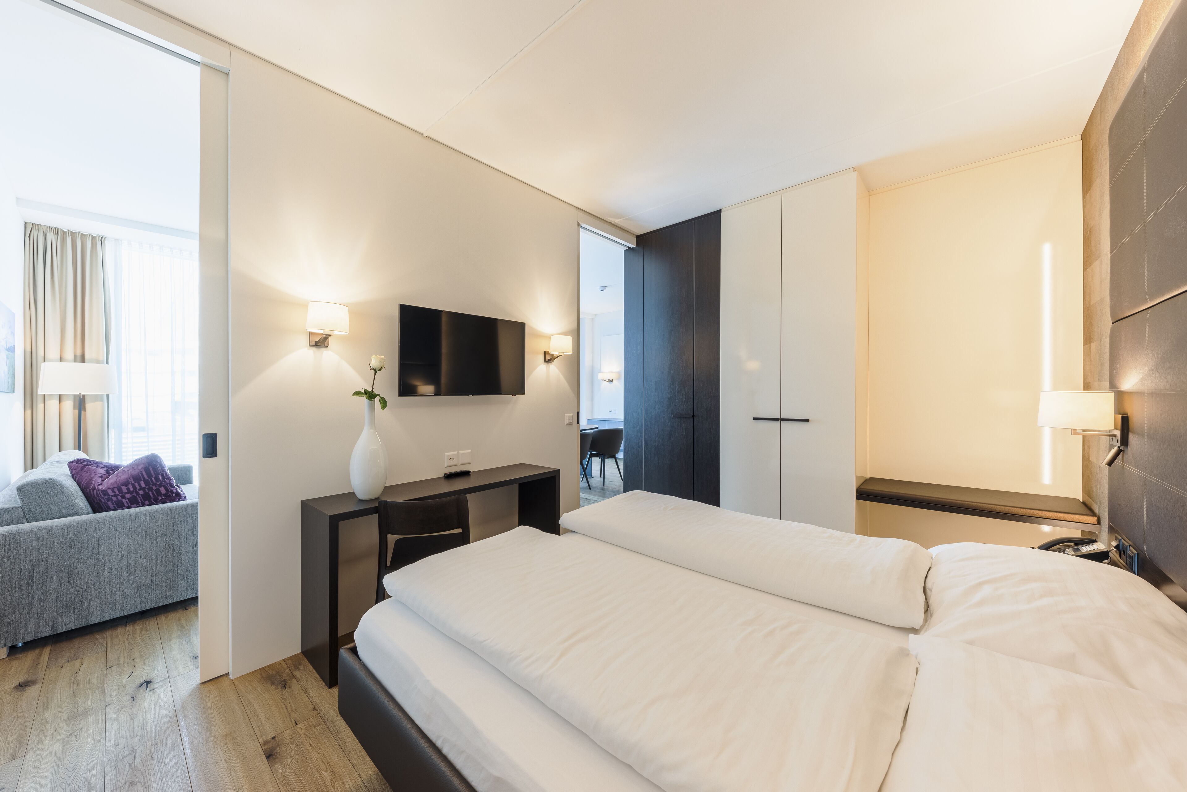 Una habitación de hotel moderna con una cama grande, un escritorio con lámpara, un televisor de pantalla plana y un sofá.