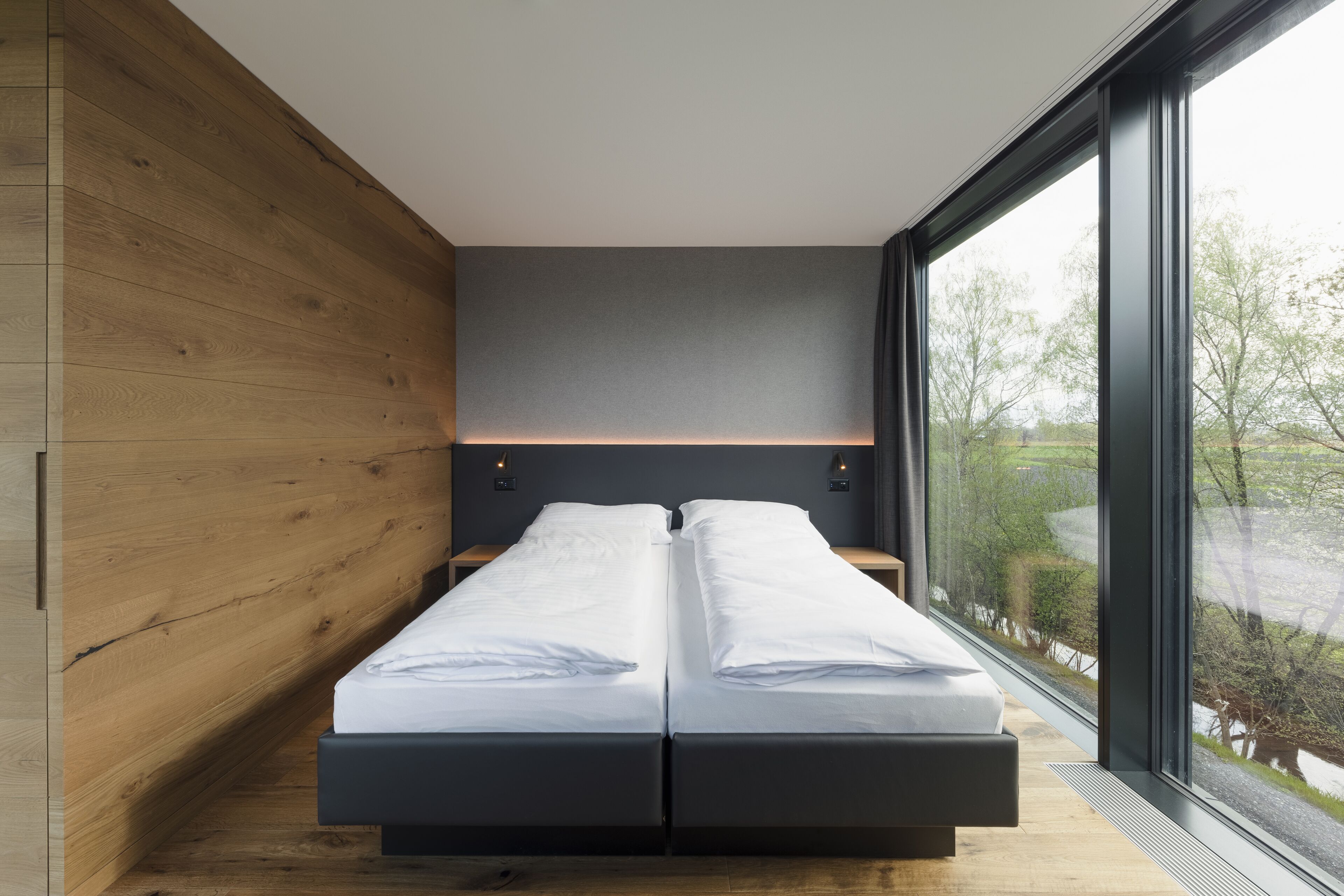 Quarto moderno com teto inclinado de madeira, uma janela grande e uma cama com roupa de cama branca.