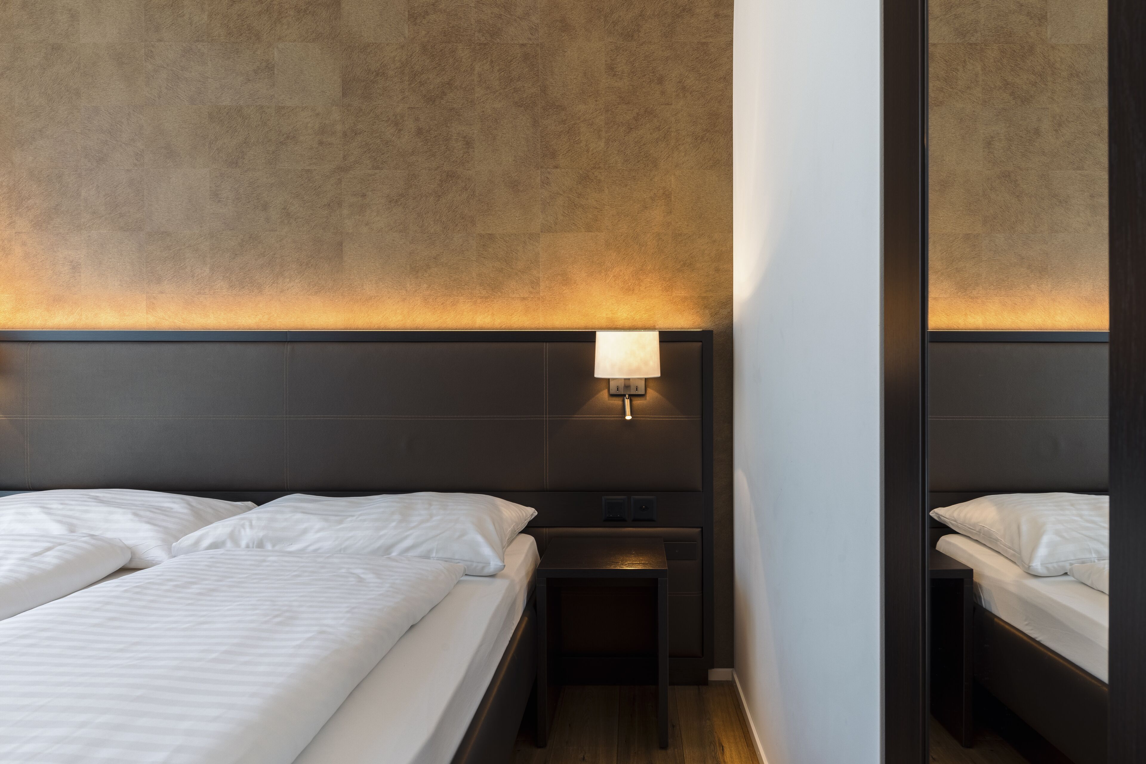 A hotel room with two beds, a nightstand with a lamp, and a mirror.