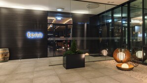 A modern hotel entrance with a 'tenn' sign, a glass facade, and a seating area with a planter and decorative lighting. - Hotel Kommod (Ruggell)