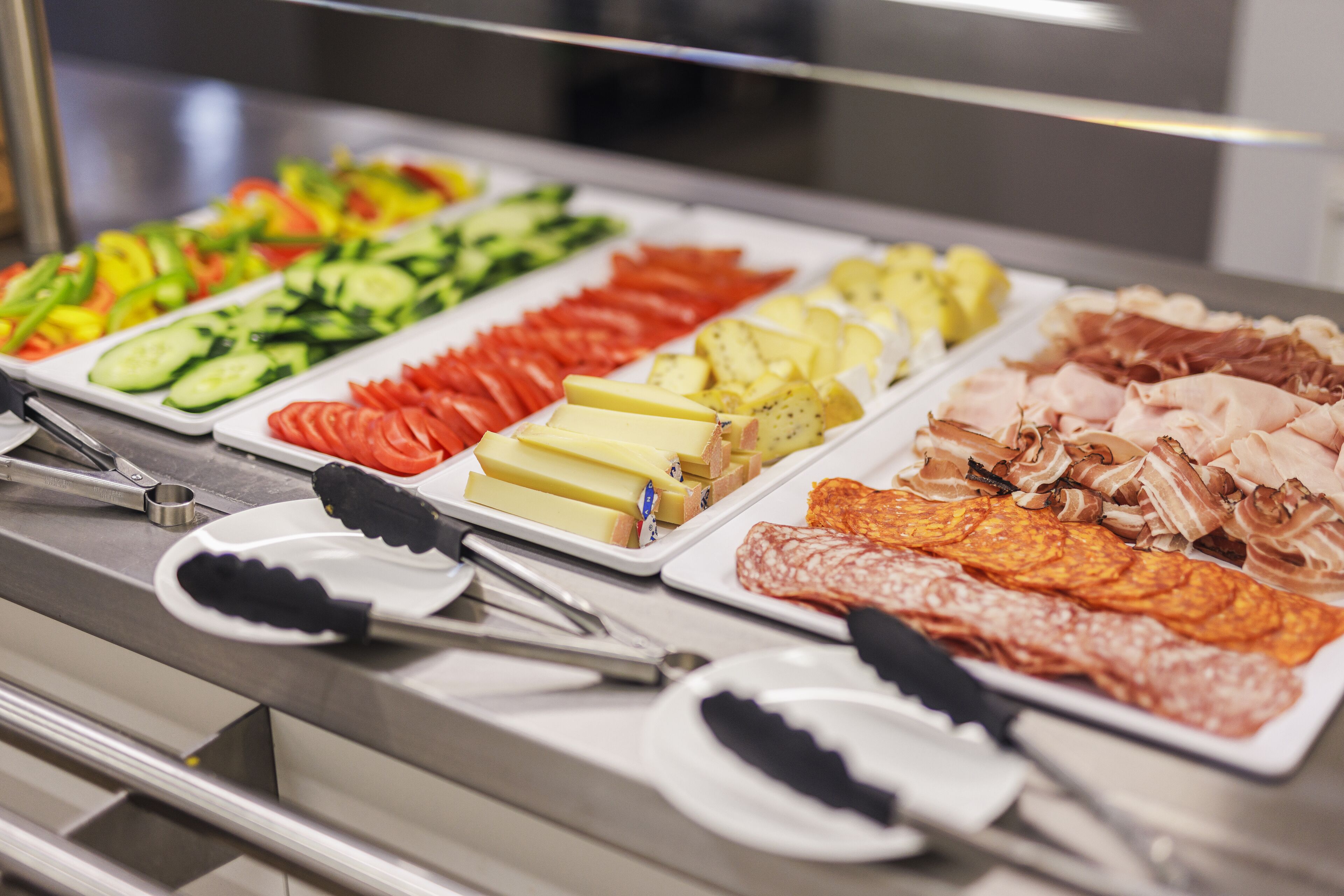 Un bufé con diversas opciones de comida, incluyendo verduras, quesos y carnes.